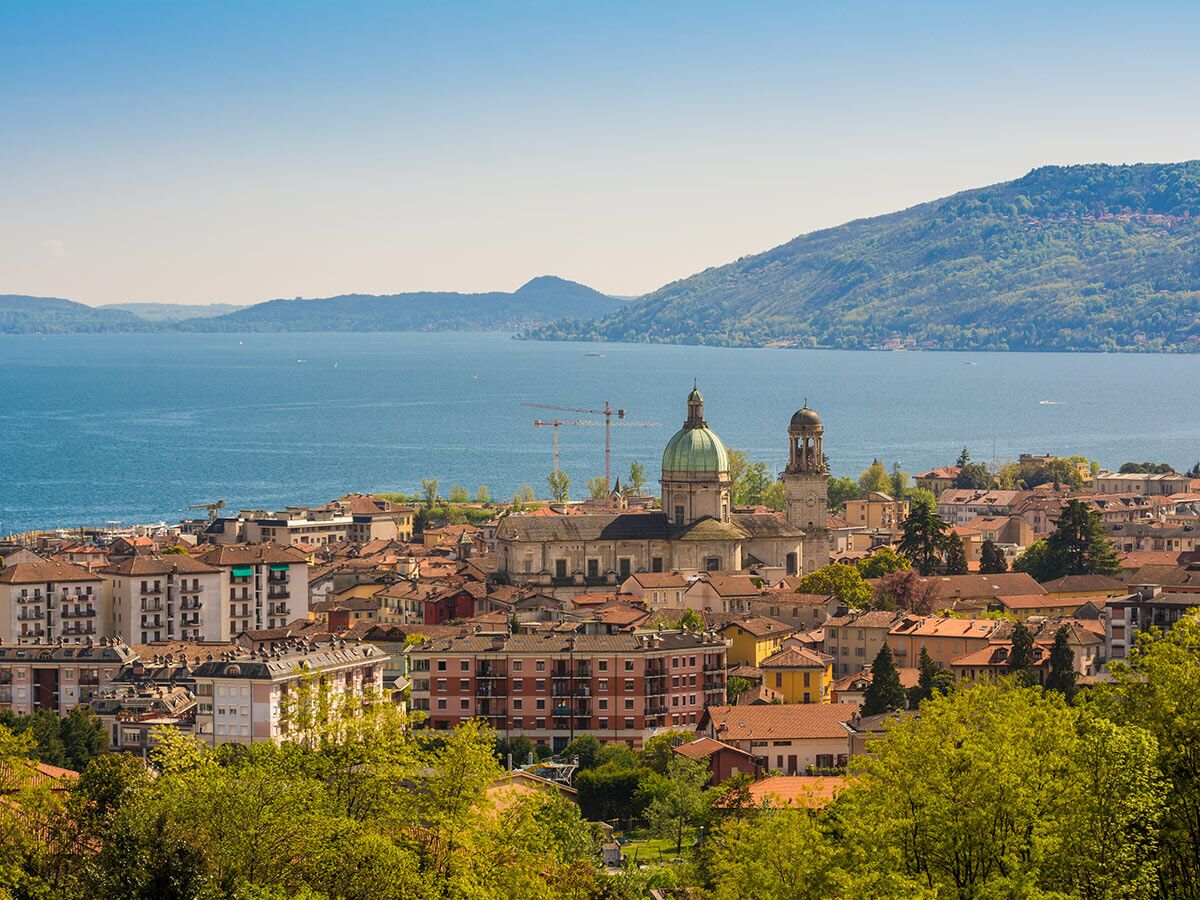 Panoramablick auf Verbania am Lago Maggiore mit grüner Kuppelkirche, Glockenturm, See und Bergen unter blauem Himmel.