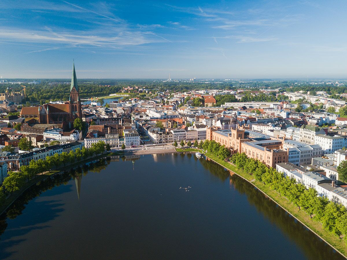 Luftaufnahme von Schwerin mit dem Pfaffenteich, dem Schweriner Dom und der Altstadt unter blauem Himmel.