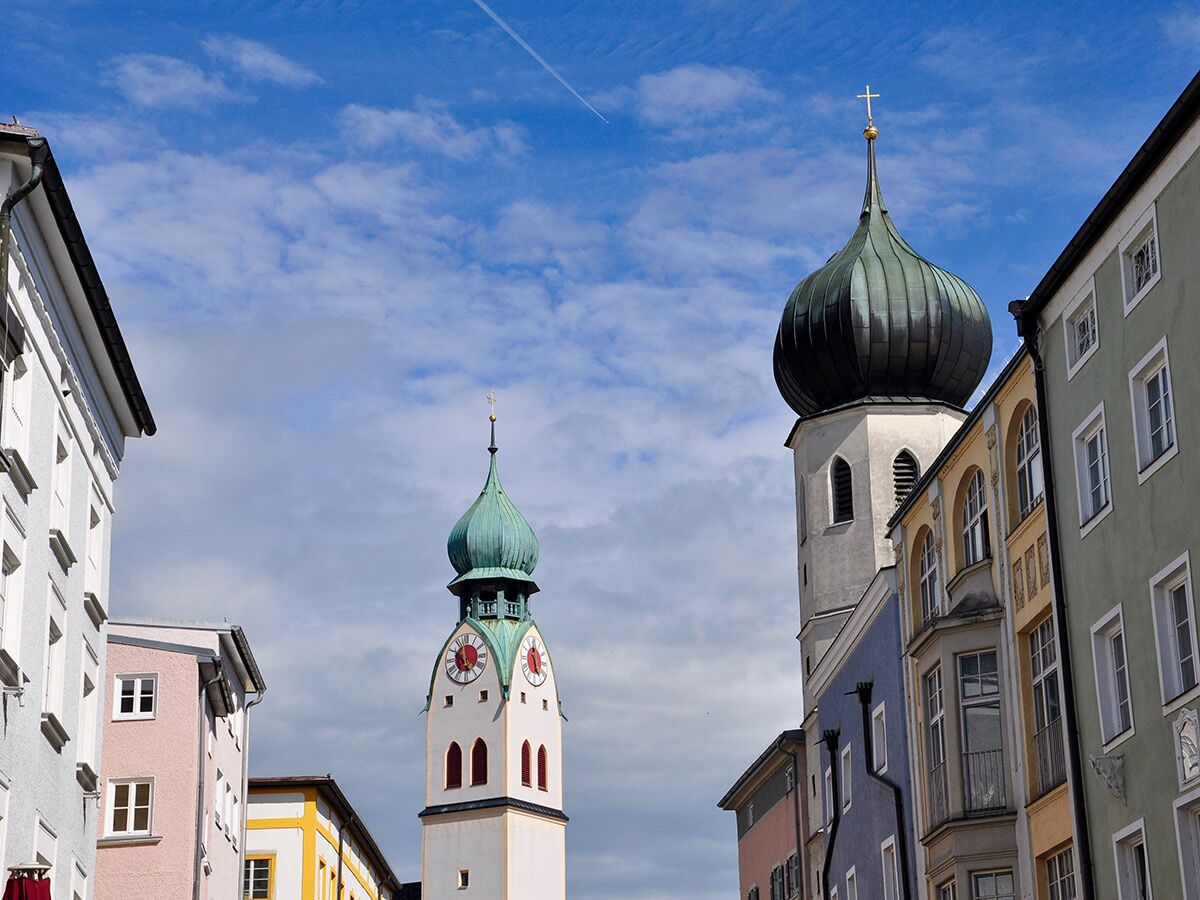 Zwei barocke Kirchtürme mit charakteristischen Zwiebelkuppeln ragen über bunte, historische Gebäude unter blauem Himmel auf.