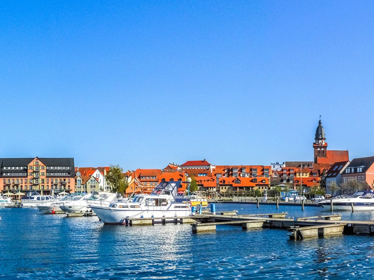 Malerische Hafenstadt mit vielen Booten, Yachten, historischen Gebäuden und einem Kirchturm unter blauem Himmel.