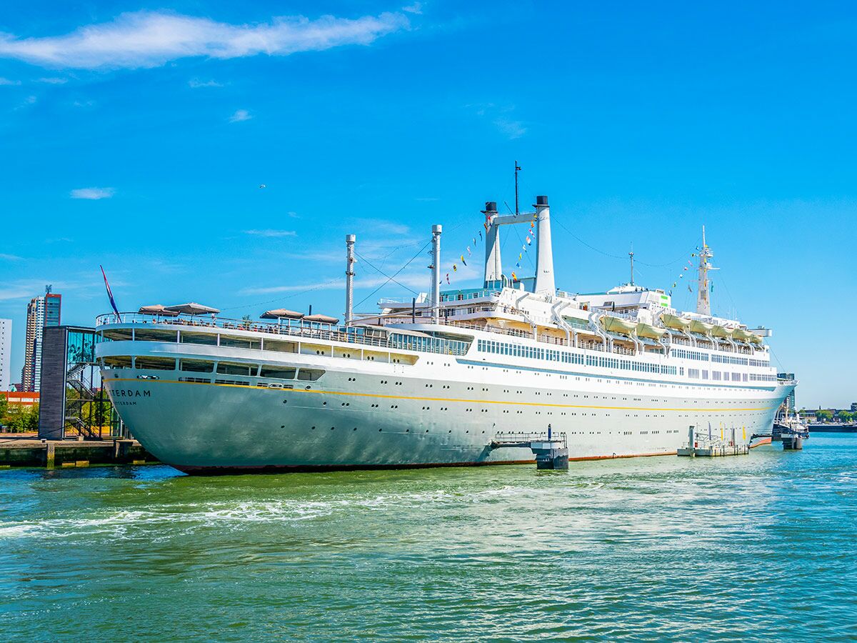 Großes Passagierschiff SS Rotterdam im Hafen, mit blauer Hülle und weißen Aufbauten unter klarem Himmel.