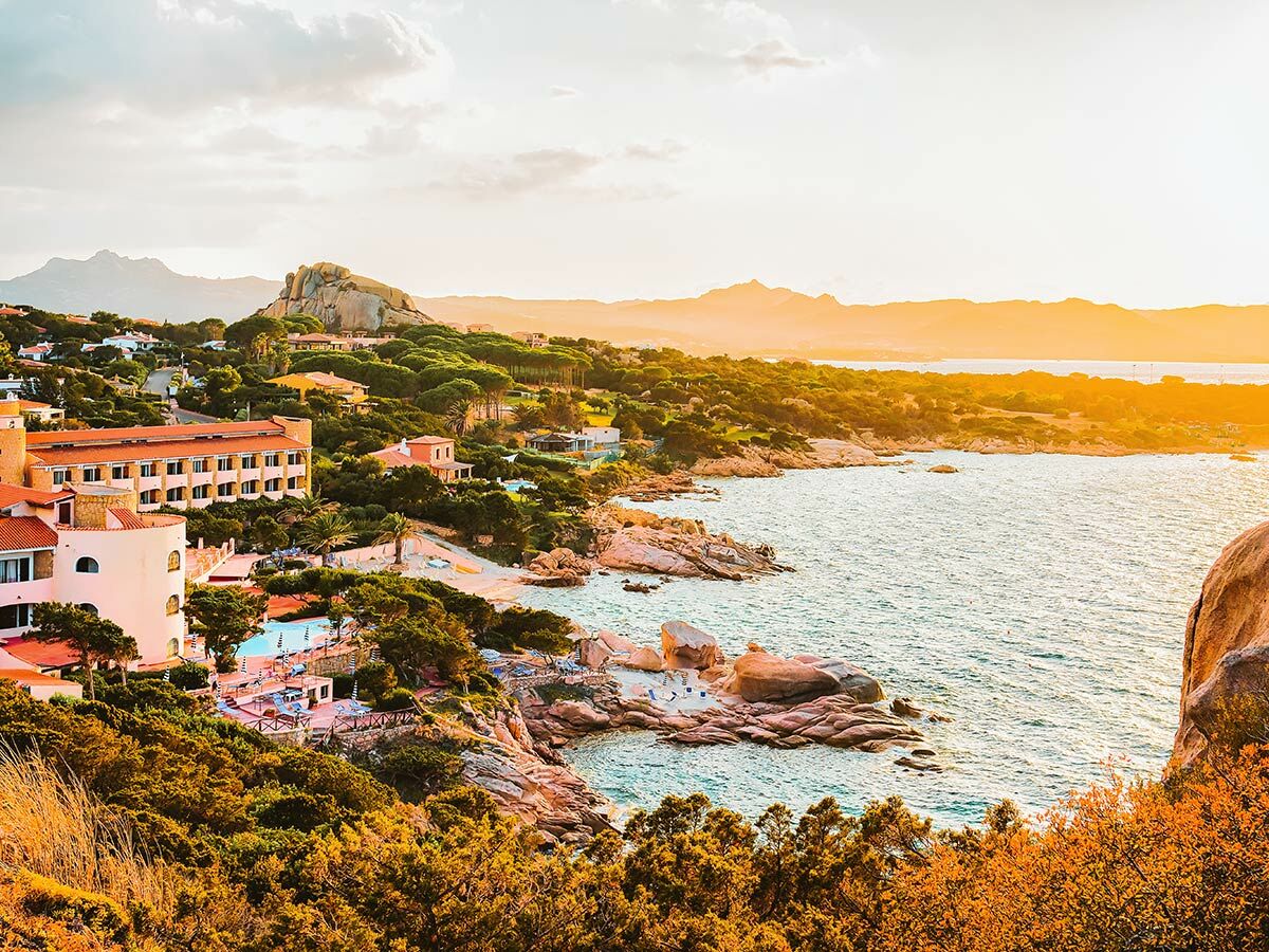 Malerisches Küstenresort mit Gebäuden, Stränden und Felsen bei goldenem Sonnenuntergang am Mittelmeer.