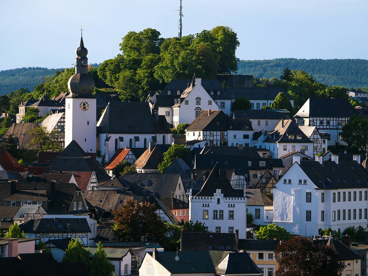 Panoramablick auf eine malerische deutsche Stadt mit weißer Kirche, Fachwerkhäusern und grünen Hügeln unter blauem Himmel.