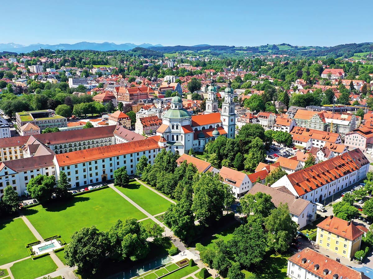 Luftaufnahme von Passau mit St. Stephan Dom, historischen Gebäuden, grünen Gärten und Bergen im Hintergrund.