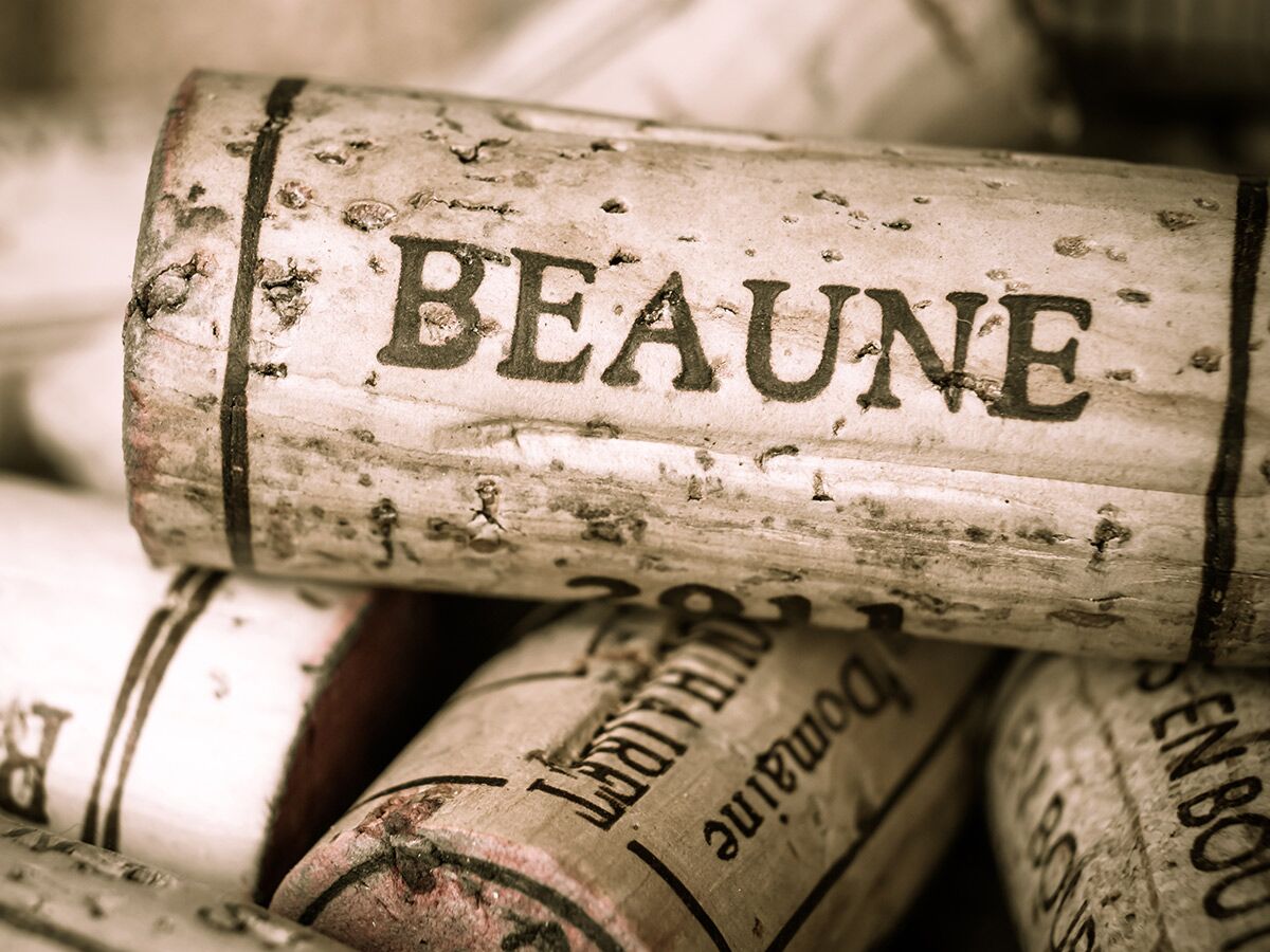 Nahaufnahme eines alten Weinkorkens mit der Aufschrift 'BEAUNE', umgeben von weiteren Korken in Sepia-Tönung.