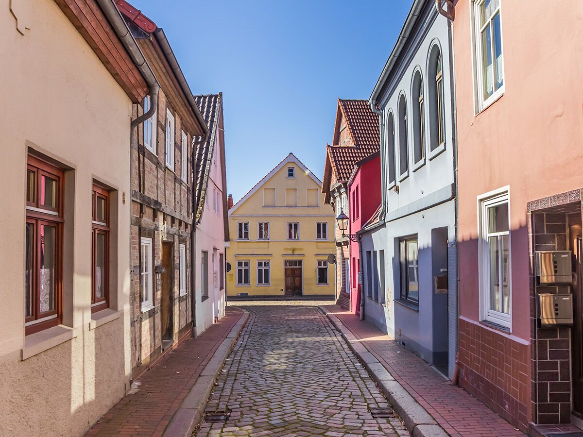 Enge Gasse mit Kopfsteinpflaster, gesäumt von bunten, historischen Fachwerkhäusern unter blauem Himmel in der Altstadt.