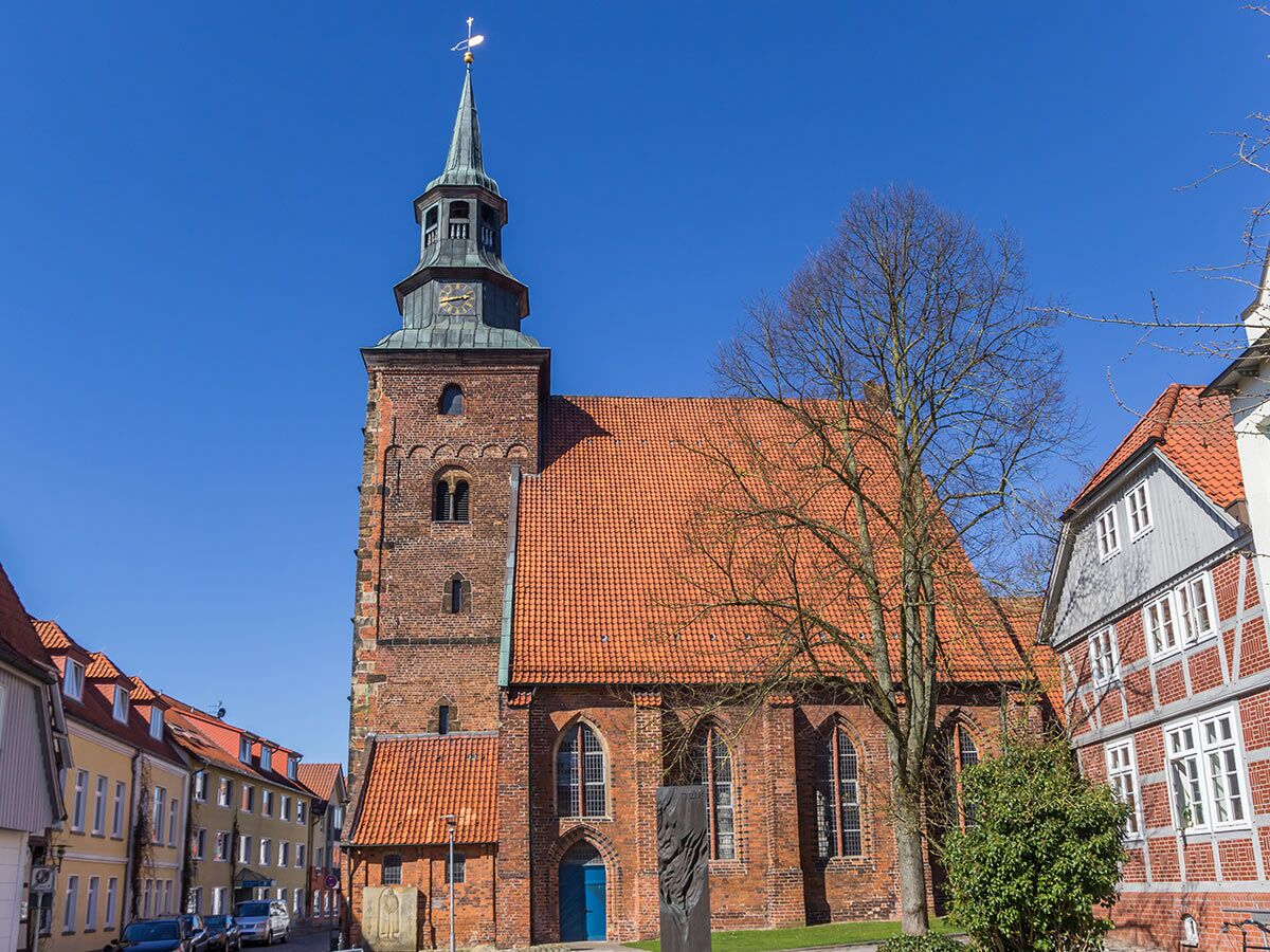 Historische Backsteinkirche mit hohem Turm, Uhr und rotem Dach in einer europäischen Altstadt an sonnigem Tag.