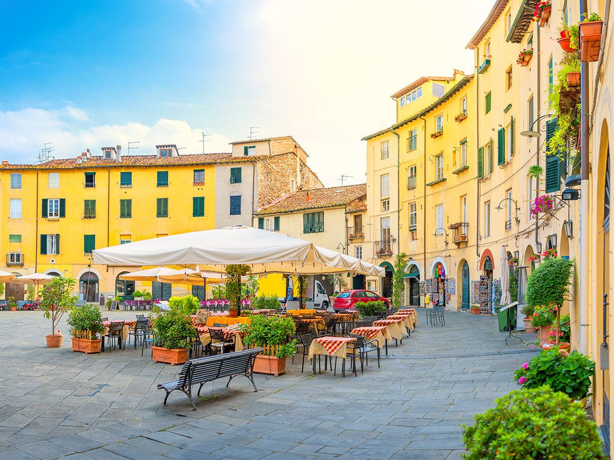 Malerischer Marktplatz in Lucca, Italien, mit sonnigen Straßencafés, farbenfrohen Gebäuden und blauem Himmel.