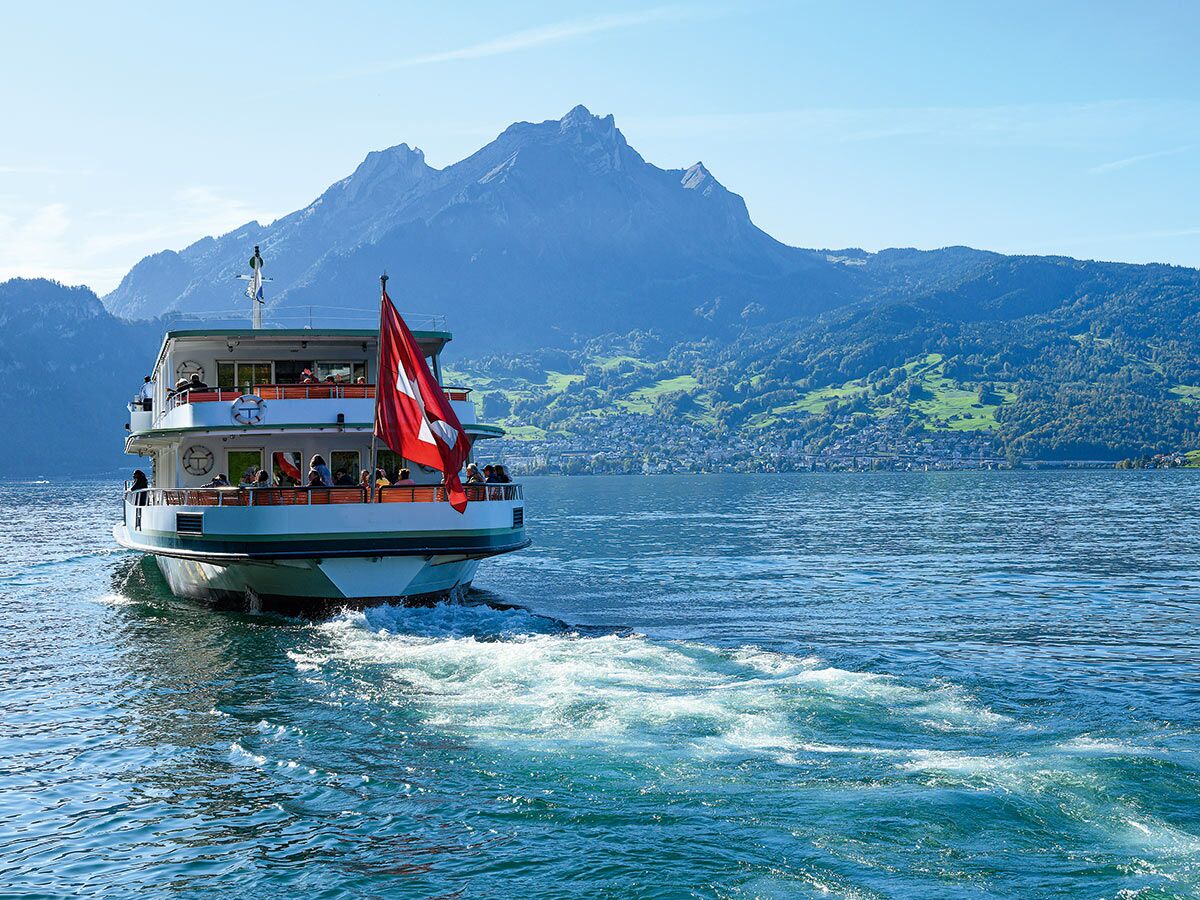 Ein Passagierboot mit Schweizer Flagge fährt auf dem blauen Vierwaldstättersee, umgeben von grünen Bergen.