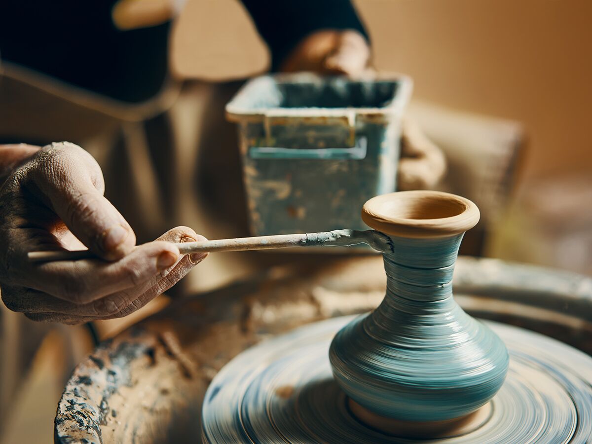 Nahaufnahme: Töpfer bemalt türkisfarbene Tonvase auf Töpferscheibe mit Pinsel. Kreative Handwerkskunst.