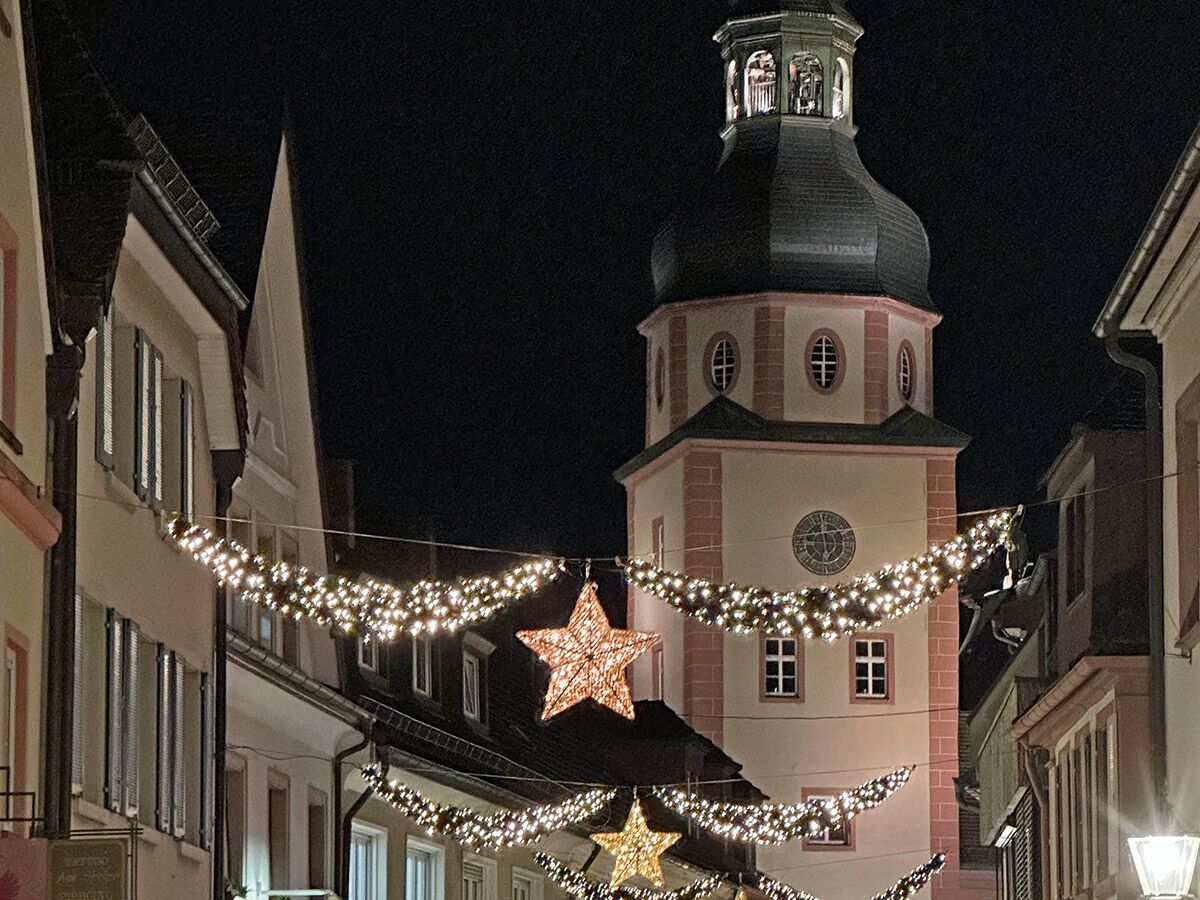 Festlich beleuchtete Altstadtgasse bei Nacht mit Weihnachtsbeleuchtung, leuchtenden Sternen und einem hohen Kirchturm im Hintergrund.