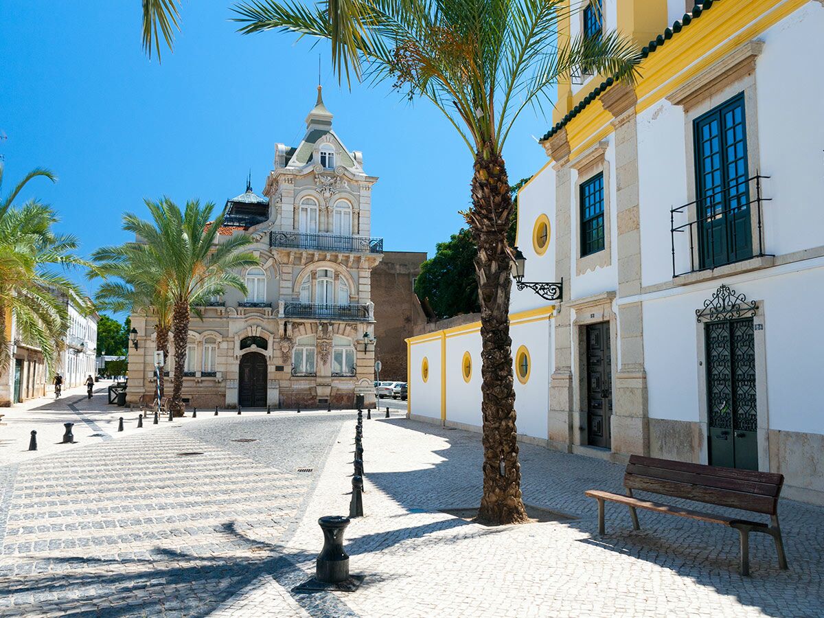 Historisches Palacete Belmarço Gebäude in Faro, Portugal, mit Palmen und Kopfsteinpflasterstraße unter blauem Himmel.