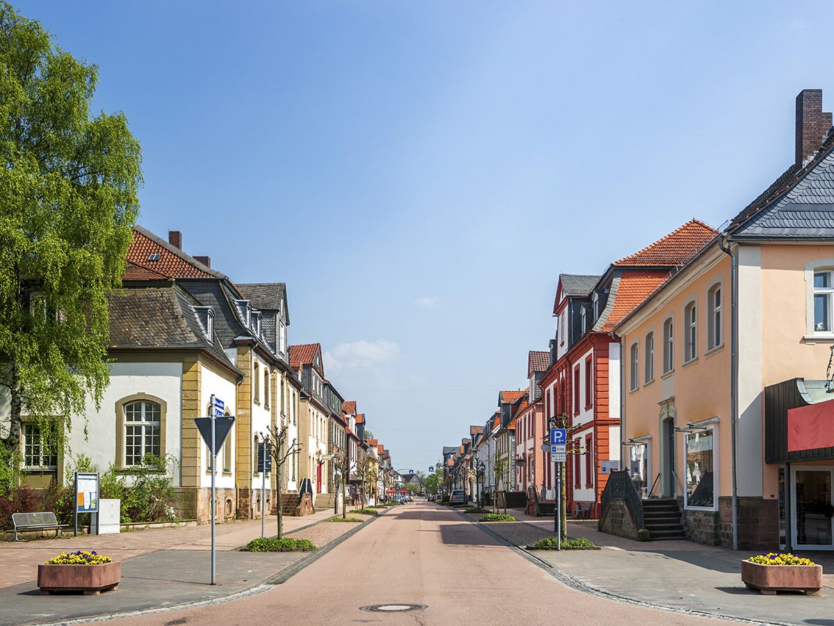 Sonnige Straße in einer deutschen Kleinstadt, gesäumt von historischen Gebäuden mit bunten Fassaden und Dächern unter blauem Himmel.