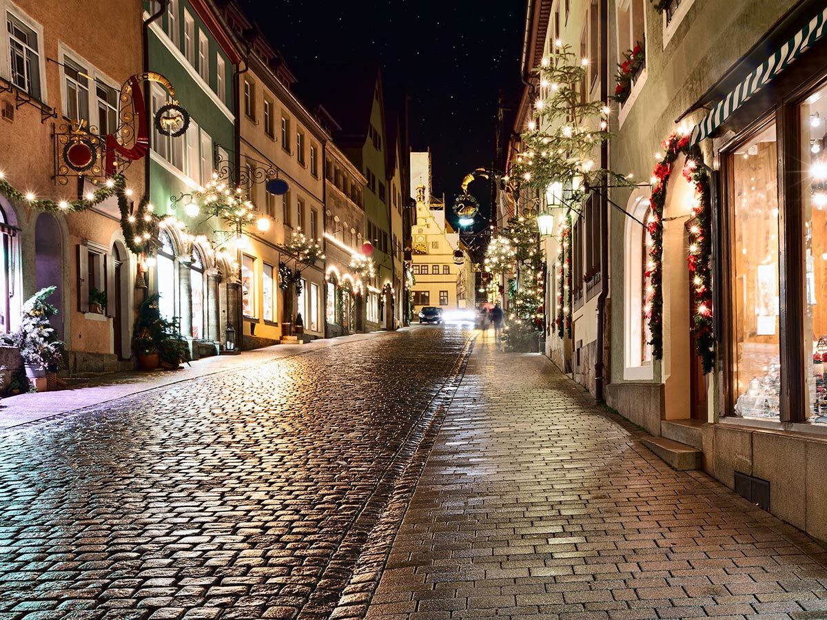 Festlich beleuchtete Altstadtgasse mit Kopfsteinpflaster, Geschäften und Weihnachtsdekorationen unter sternenklarem Nachthimmel.