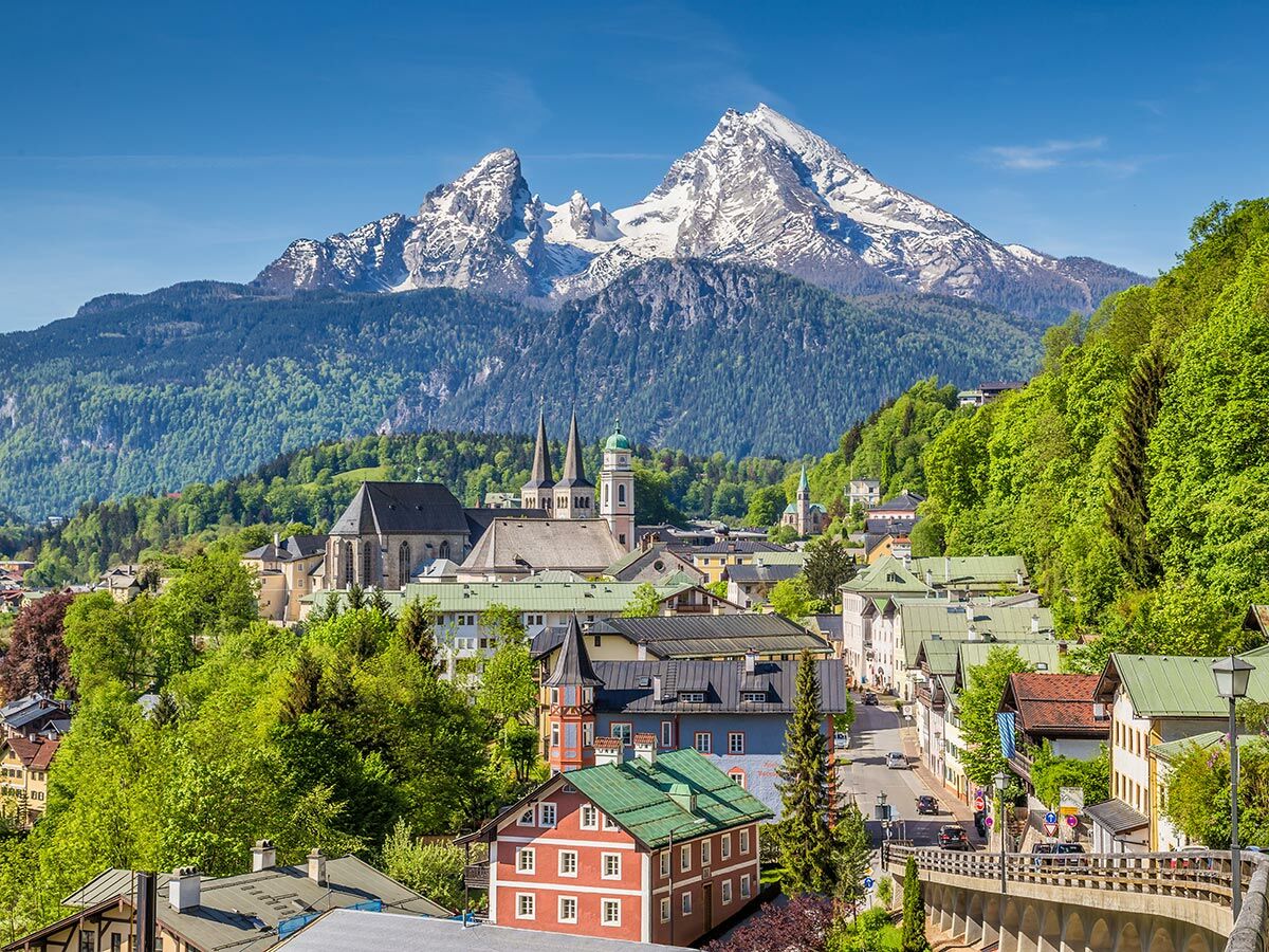 Panoramablick auf Berchtesgaden mit majestätischem, schneebedecktem Watzmann, grünen Wäldern, Kirchen und Häusern.