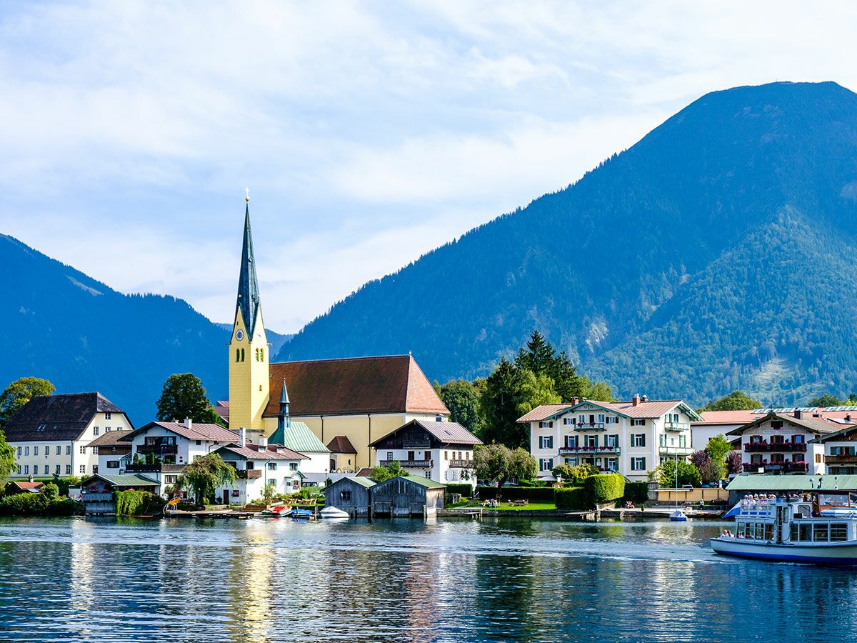 Malerisches bayerisches Dorf am Tegernsee mit Kirchturm, traditionellen Häusern, Bergen und Booten auf dem See.