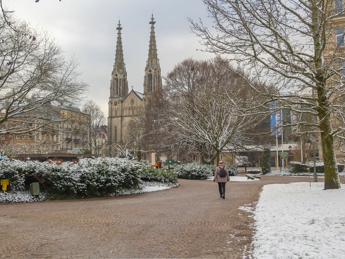 Winterlandschaft in Freiburg mit verschneitem Park, Bäumen und der imposanten St. Karl Borromäus Kirche im Hintergrund.