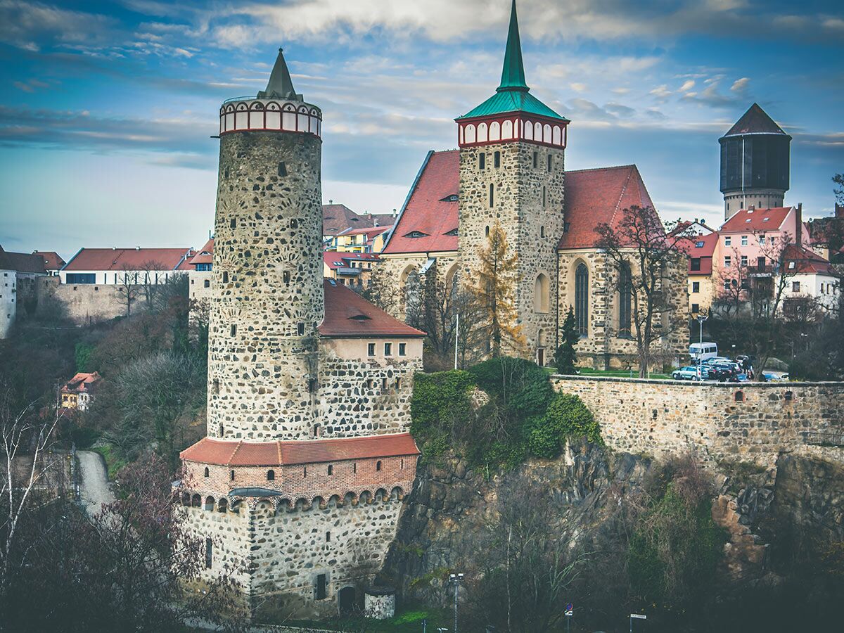 Historische Stadtansicht von Bautzen mit dem markanten Reichenturm, der Liebfrauenkirche und weiteren alten Gebäuden unter bewölktem Himmel.