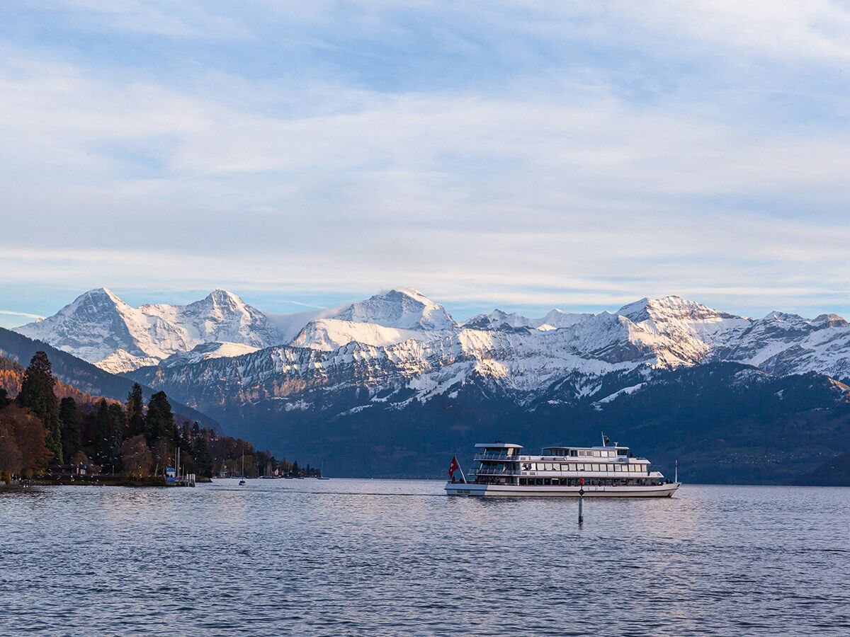 Ein großes Passagierschiff fährt auf einem Schweizer See vor einer beeindruckenden Kulisse schneebedeckter Alpen im Herbst.