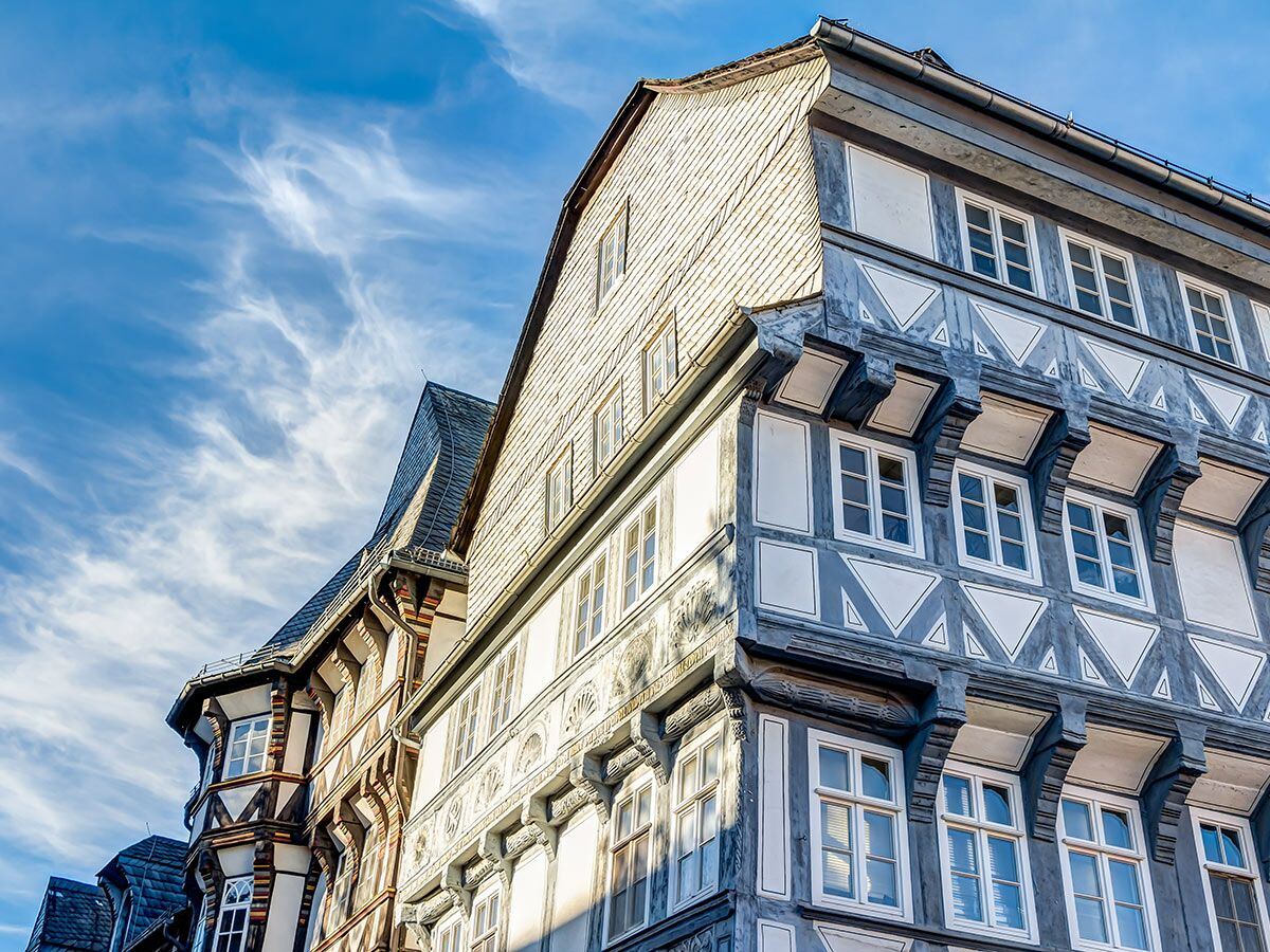 Ansicht von unten auf prächtige, detaillierte Fachwerkhäuser mit Schieferdächern und traditioneller Bauweise unter blauem Himmel.