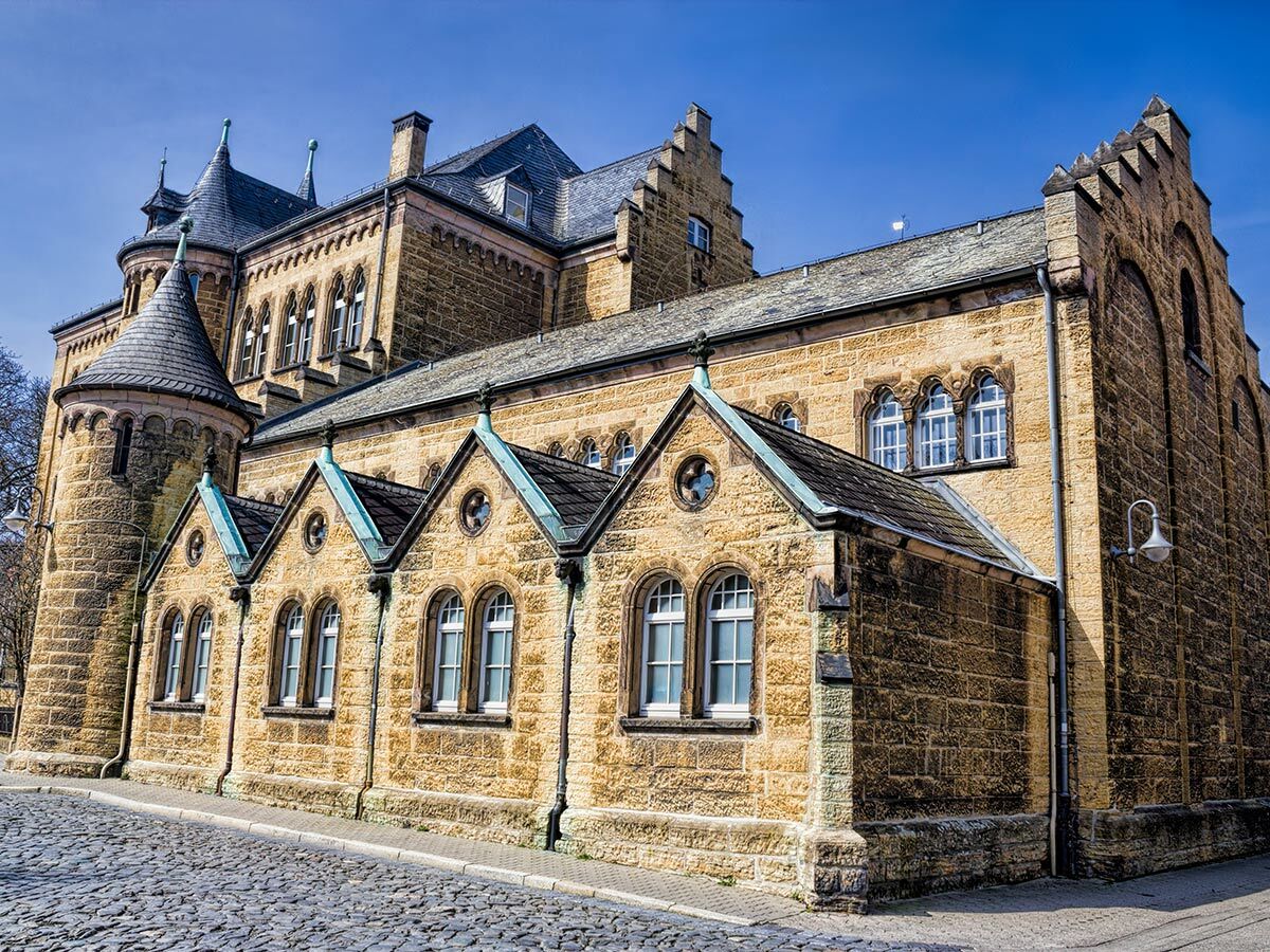 Die Kaiserpfalz Goslar, ein imposanter Steinbau im romanischen Stil, zeigt Türme, Giebel und Bogenfenster unter blauem Himmel.