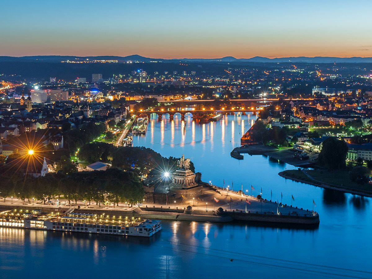 Luftaufnahme von Koblenz Deutsches Eck bei Nacht, wo Mosel und Rhein zusammenfließen, beleuchtete Stadt und Brücken.