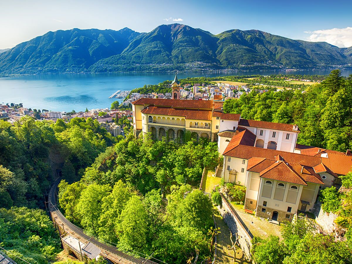 Panoramablick auf das Wallfahrtskloster Madonna del Sasso in Locarno, Schweiz, mit Lago Maggiore und Bergen im Hintergrund.
