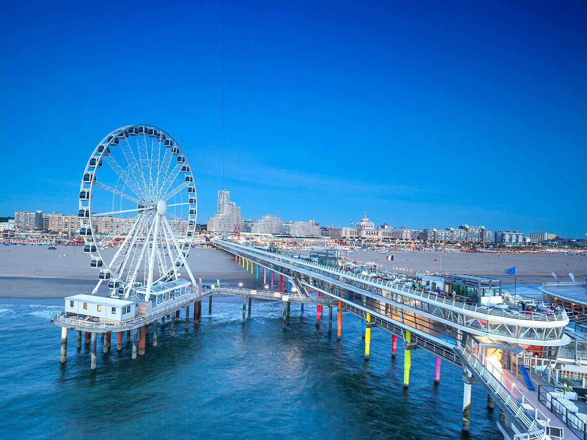 Scheveningen Pier mit Riesenrad und beleuchteter Promenade bei blauer Stunde in Den Haag, Niederlande.