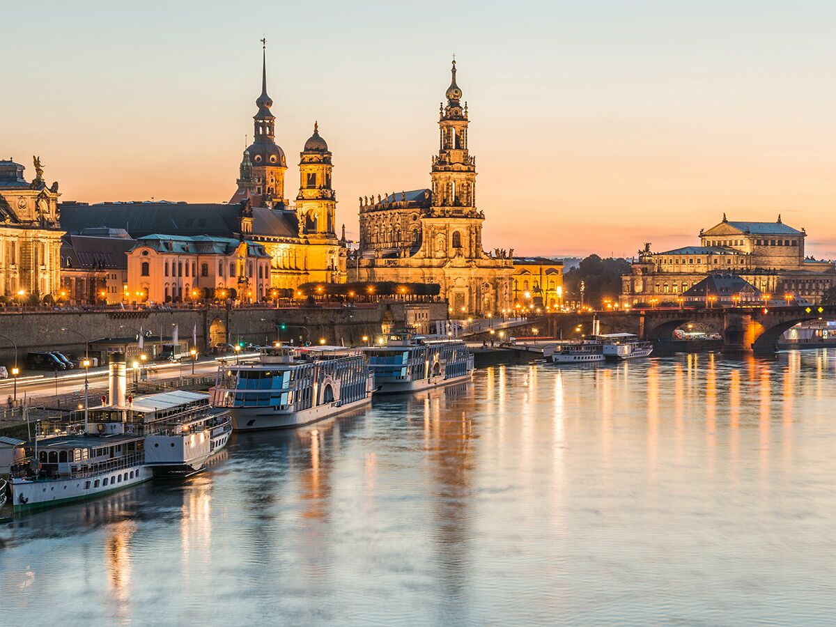 Panoramablick auf die beleuchtete Dresdner Altstadt bei Sonnenuntergang mit der Elbe, Brücke und historischen Gebäuden.