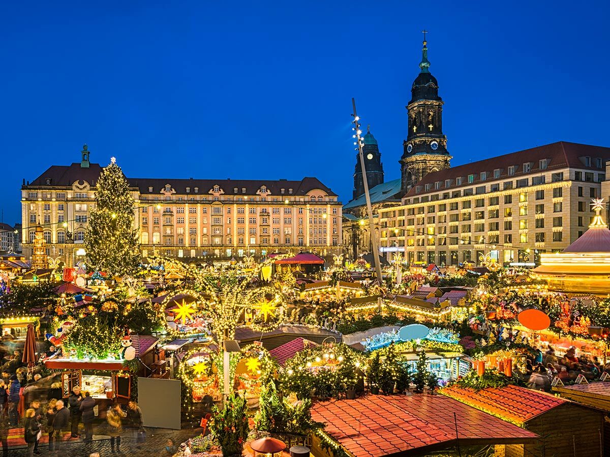 Beleuchteter Weihnachtsmarkt Dresden am Abend mit hell erleuchteten Ständen, großem Weihnachtsbaum und historischen Gebäuden im Hintergrund.