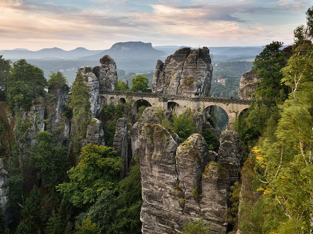 Historische Basteibrücke verbindet majestätische Sandsteinfelsen im Nationalpark Sächsische Schweiz, umgeben von dichtem Wald.