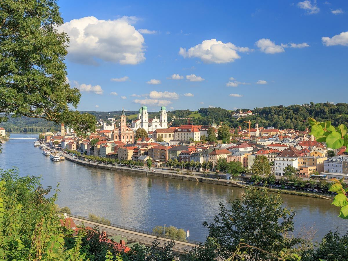Panoramablick Passau Altstadt mit farbenfrohen Gebäuden am Flussufer, St. Stephansdom und blauer Himmel.