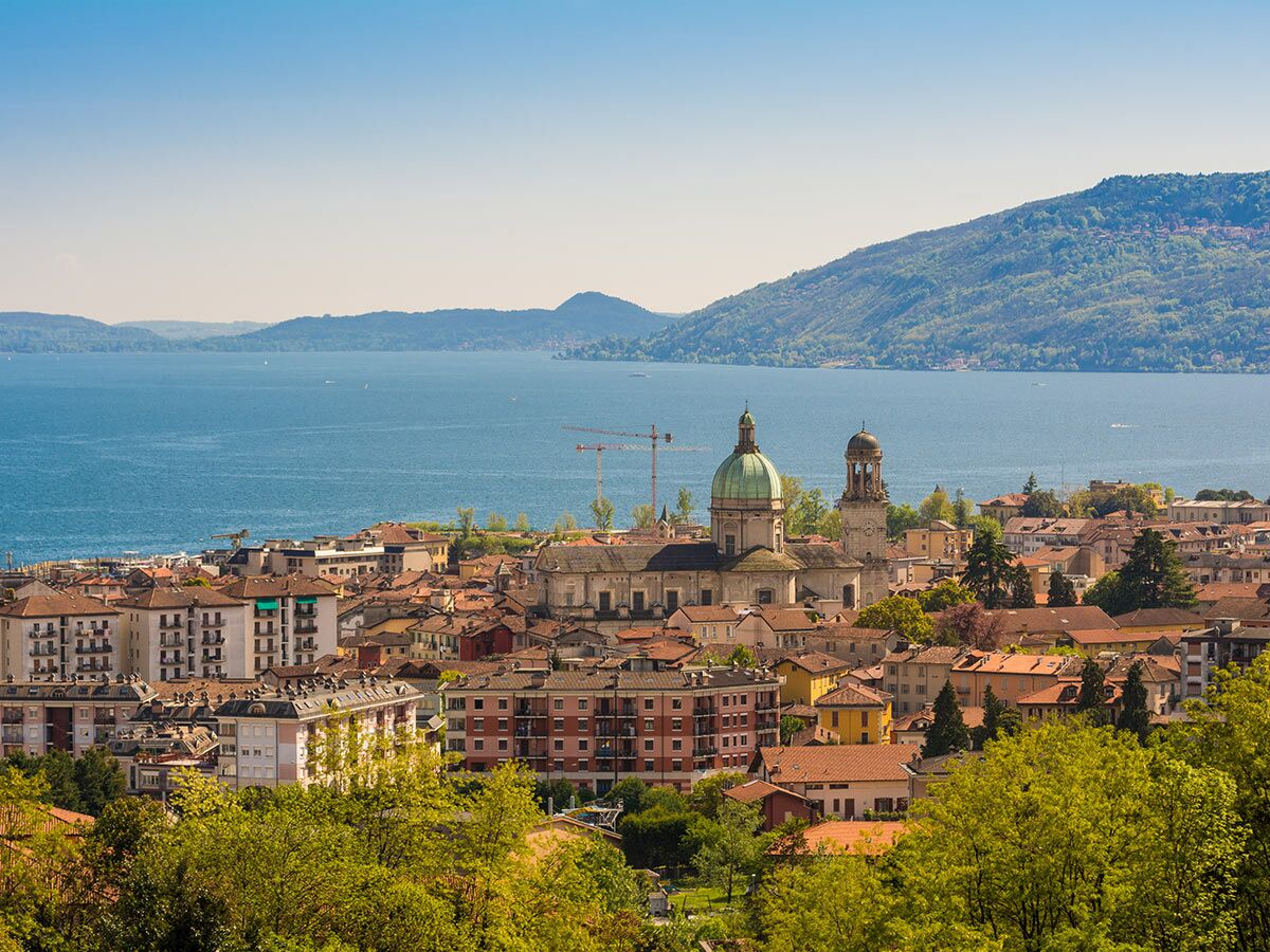 Panorama einer malerischen Stadt am See mit grüner Domkuppel, historischen Gebäuden und bewaldeten Bergen.
