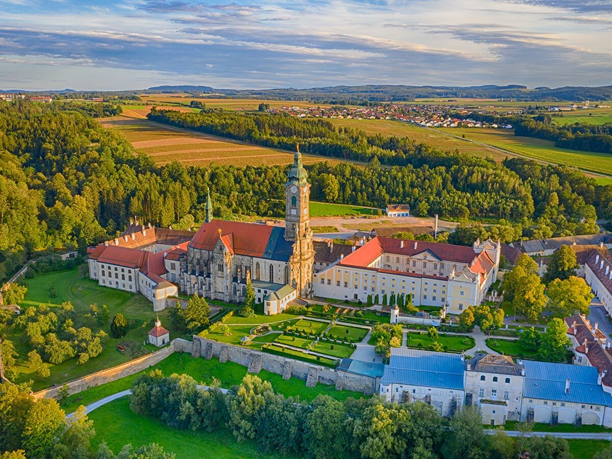 Luftaufnahme des historischen Stifts Melk in Österreich mit Barockkirche, Klostergebäuden, Gärten, Wäldern und Feldern.
