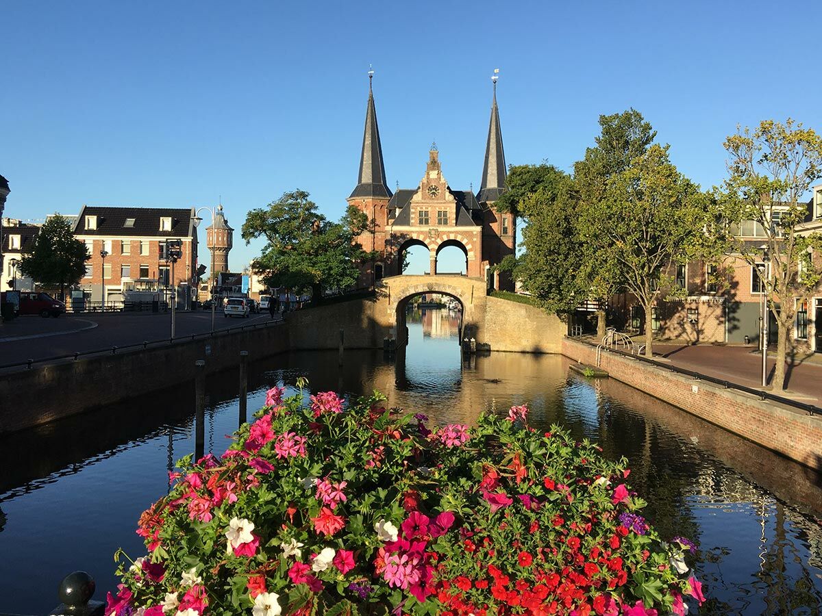Historische Waterpoort in Sneek, Niederlande, mit Türmen, Brücke über Kanal und bunten Blumen im Vordergrund.