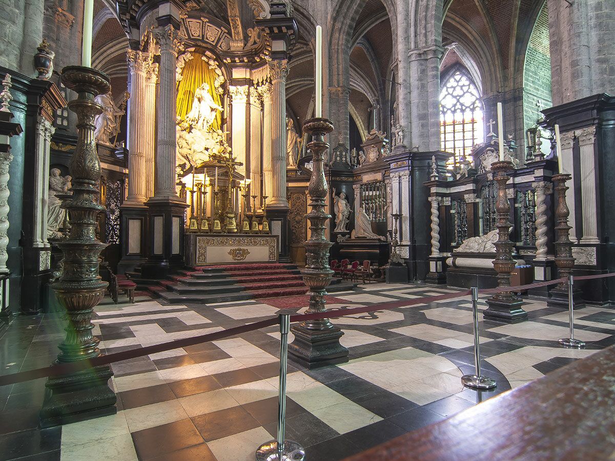 Prachtvolle Innenansicht einer barocken Kirche mit goldenem Hochaltar, Skulpturen, verzierten Säulen und schwarz-weißem Fliesenboden.