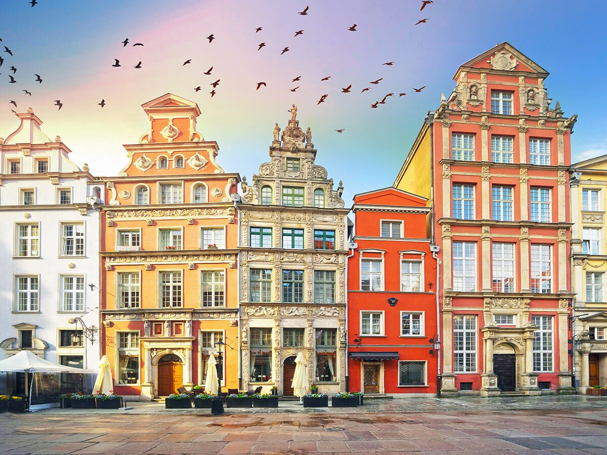 Reihen bunter historischer Gebäude am Długi Targ in Gdańsk an einem sonnigen Tag, mit Vögeln am Himmel.
