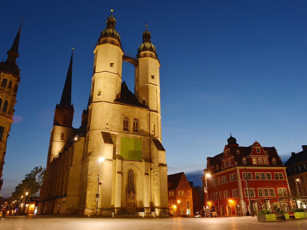 Die beleuchtete Marktkirche Unser Lieben Frauen in Halle (Saale) mit ihren Doppeltürmen bei blauer Stunde am Abend.