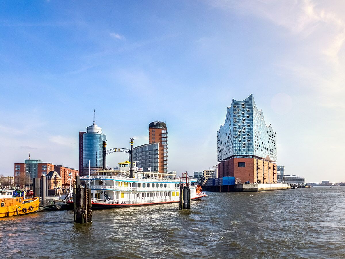Panoramablick auf die Hamburger Elbphilharmonie und den Hafen mit einem Raddampfer unter blauem Himmel.