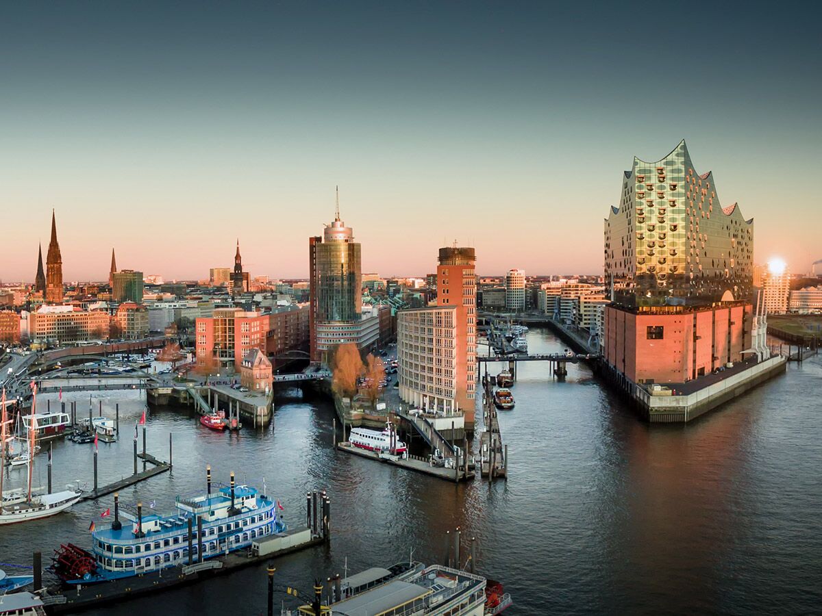 Panoramablick auf Hamburg HafenCity bei Sonnenuntergang mit der Elbphilharmonie, historischen Kirchen und Booten im warmen Licht.