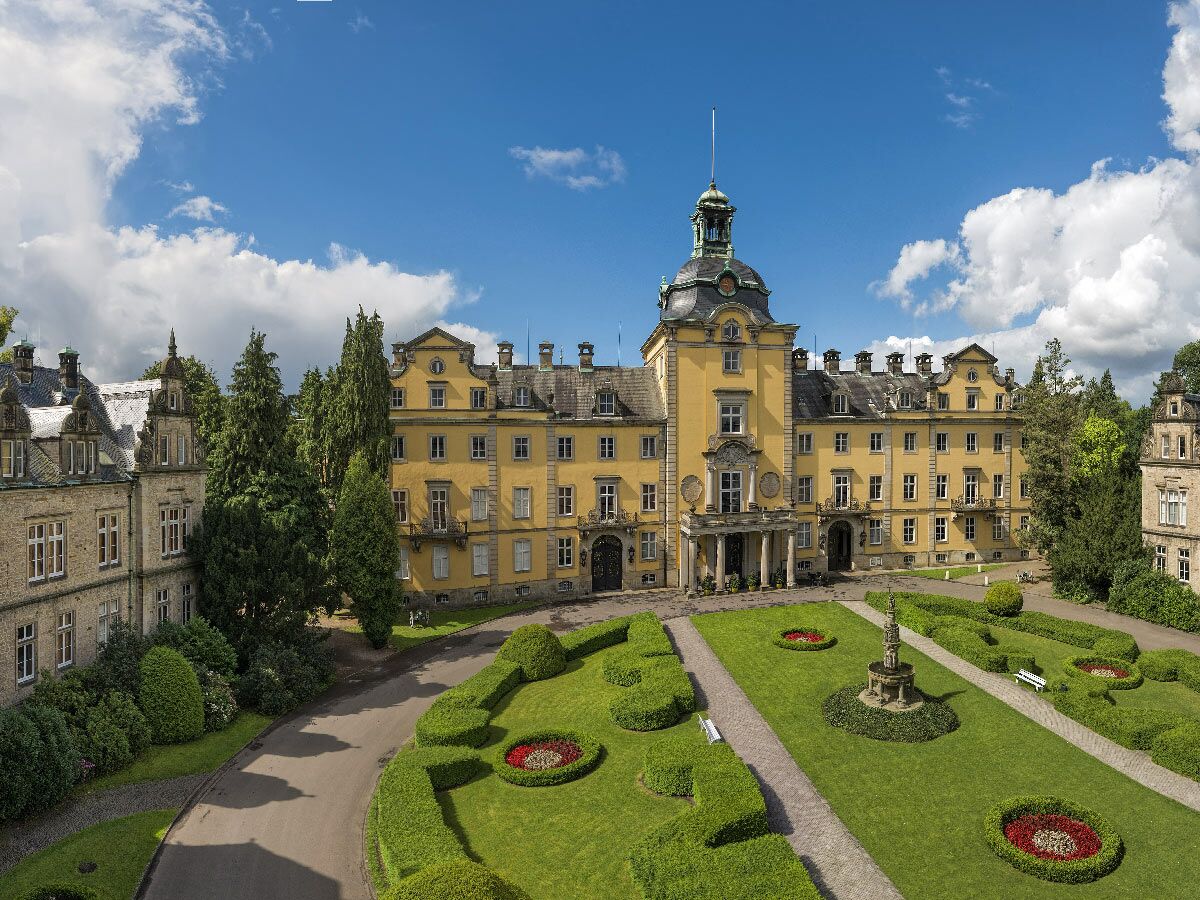 Großes gelbes Schloss Bückeburg, ein prächtiges Barockgebäude mit Turm, umgeben von einem grünen Schlossgarten mit Hecken und Brunnen.