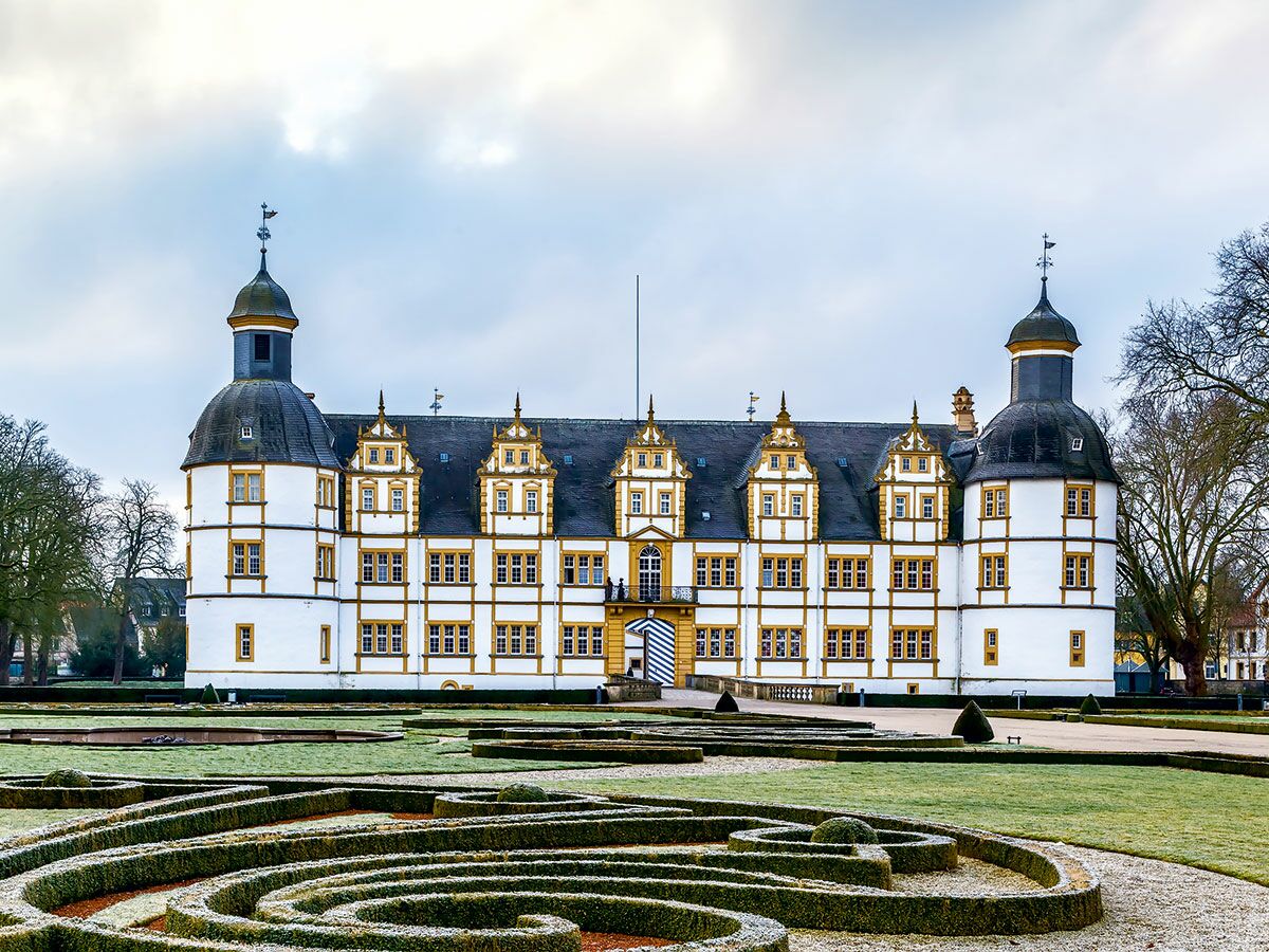 Historisches Schloss Neuhaus in Paderborn mit weißer Fassade, gelben Akzenten und zwei Türmen, umgeben von einem winterlichen Barockgarten.