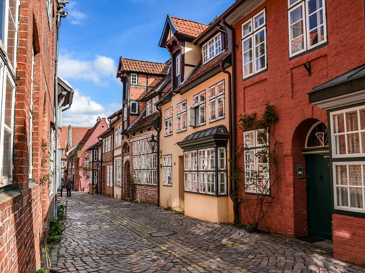 Kopfsteinpflastergasse in europäischer Altstadt mit bunten historischen Gebäuden, roten Backsteinfassaden und blauem Himmel.