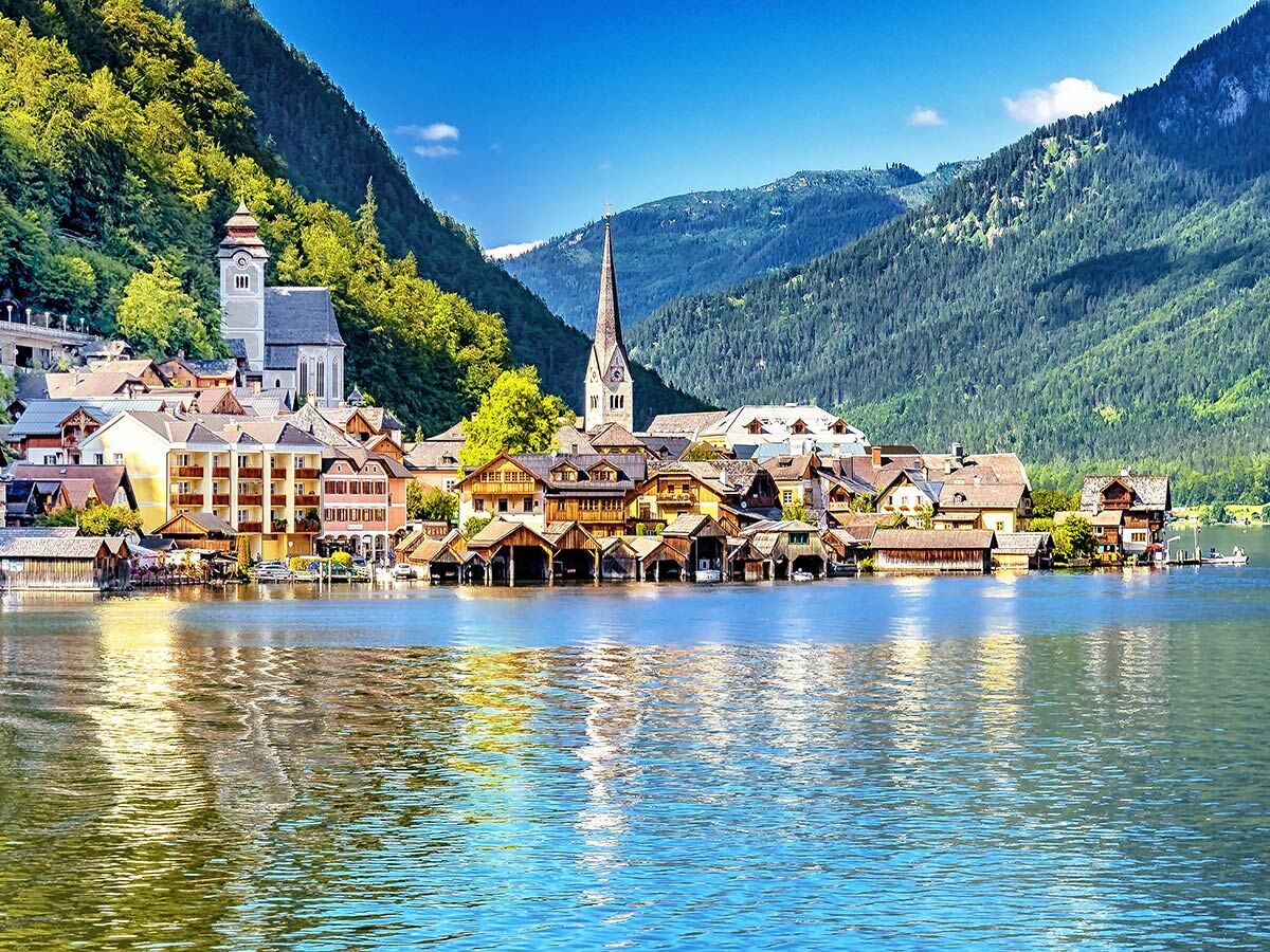 Malerisches Hallstatt Dorf mit Kirchen am Hallstätter See, umgeben von grünen Bergen unter blauem Himmel.