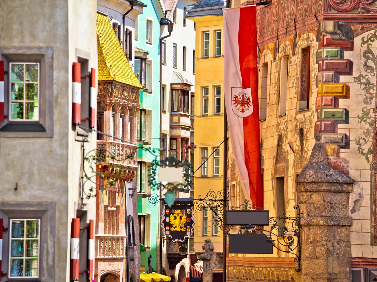 Enge Gasse in Innsbruck mit bunten historischen Häusern, goldenem Erkerdach, Tiroler Flagge und Fensterläden.