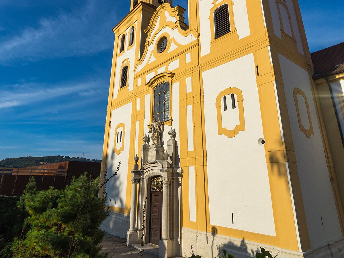 Beeindruckende Barockkirche mit strahlend gelber und weißer Fassade, kunstvollen Details, Statuen am Eingang unter blauem Himmel.