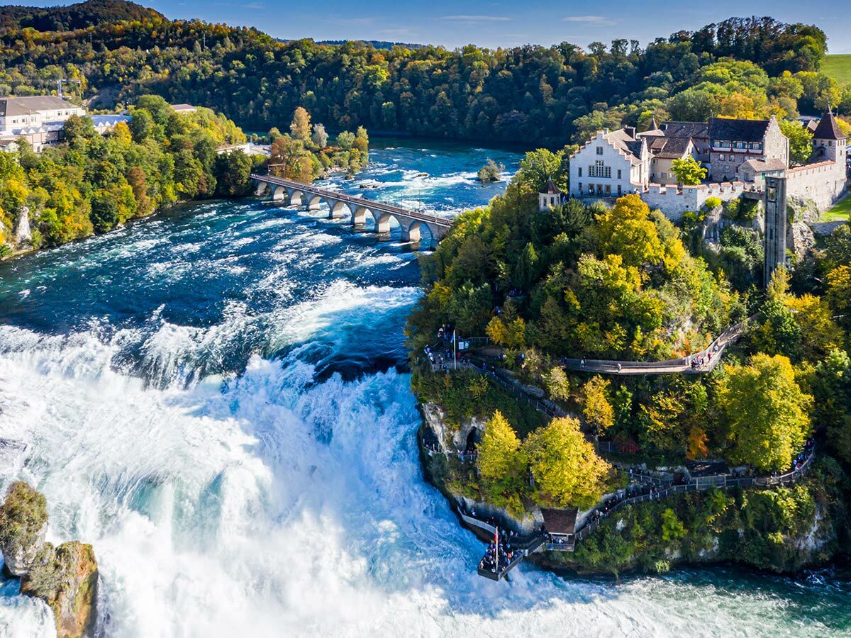 Luftbild des Rheinfalls, Schweiz, mit historischem Schloss Laufen, einer Eisenbahnbrücke und Herbstbäumen.