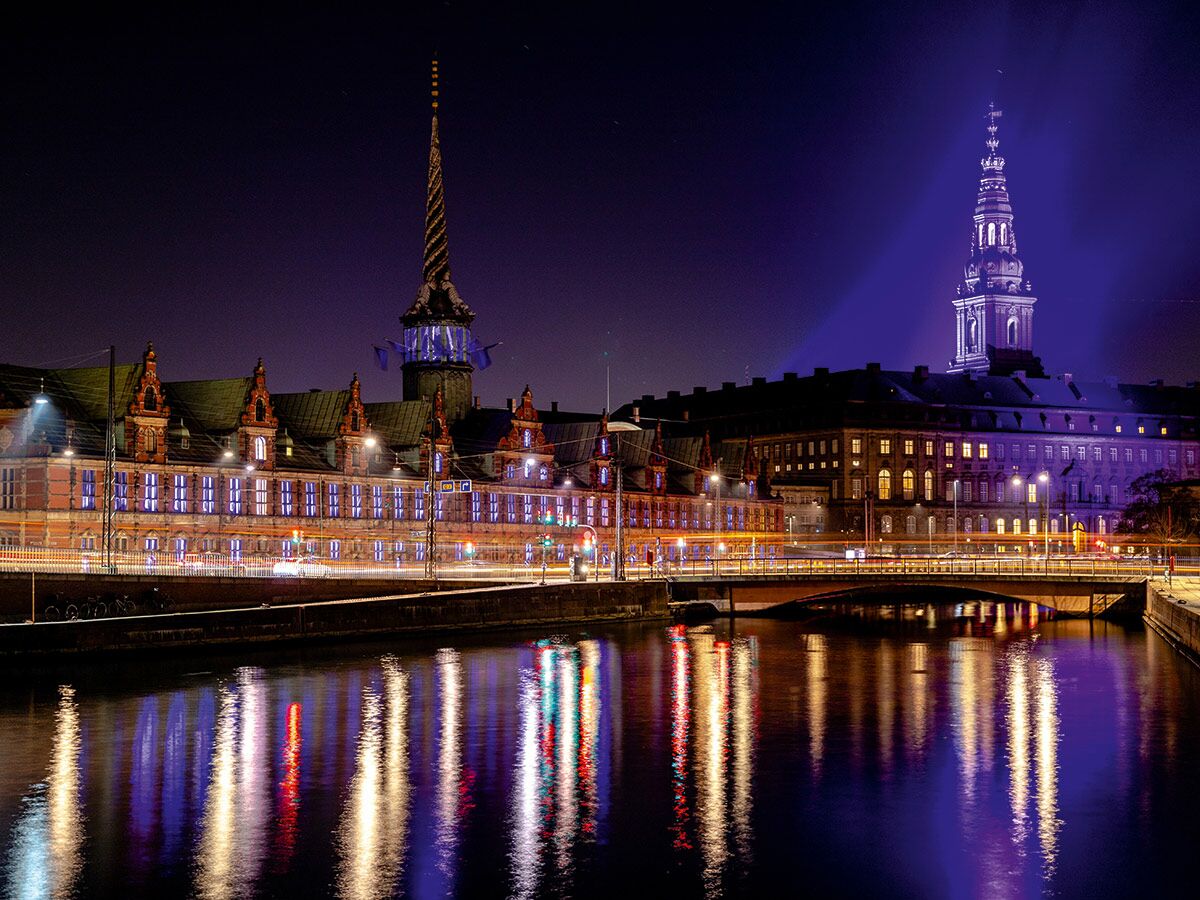 Nächtliche Ansicht von Kopenhagen mit beleuchteter Børsen und dem Turm von Schloss Christiansborg am Kanal.