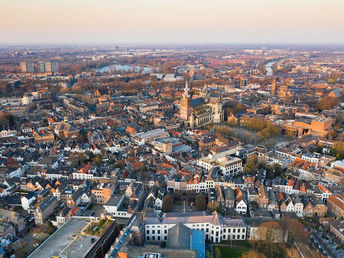 Luftaufnahme von 's-Hertogenbosch mit der Sint-Janskathedraal, historischen Gebäuden und einem See im Hintergrund bei Sonnenuntergang.