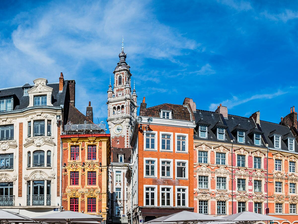 Ansicht des Grand Place in Lille mit farbenfrohen historischen Gebäuden und dem markanten Uhrturm unter blauem Himmel.